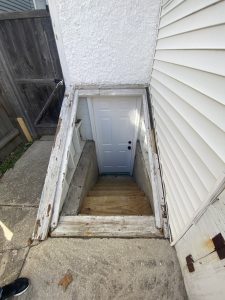 Outdoor basement stairs with damaged wood trim and exposed concrete – before repairs by Flash Handy