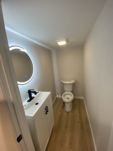 Modern bathroom with LED round mirror, white vanity, and new vinyl flooring installed by Flash Handy