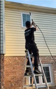 Flash Handy technician power washing second-story gutters from ladder